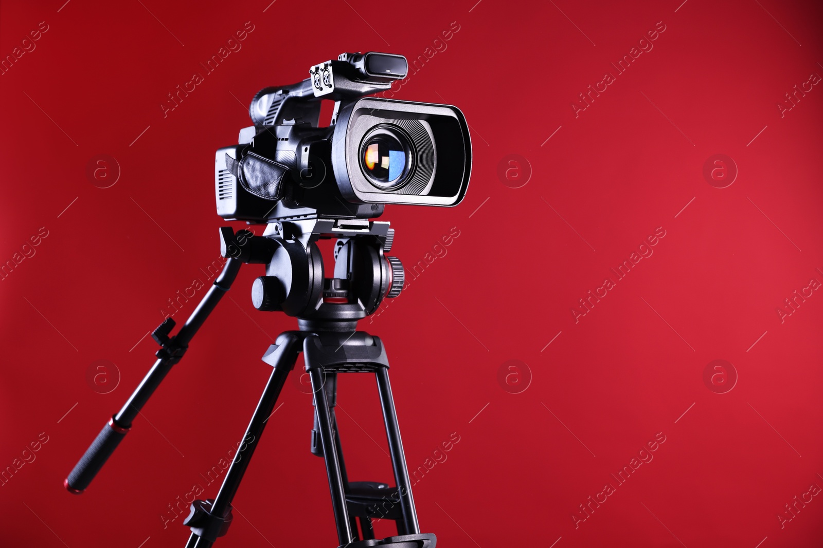 Photo of Modern video camera with tripod on red background, space for text