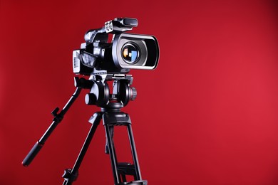 Photo of Modern video camera with tripod on red background, space for text