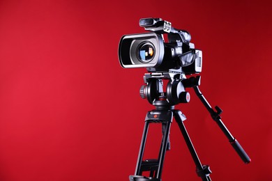 Modern video camera with tripod on red background, space for text