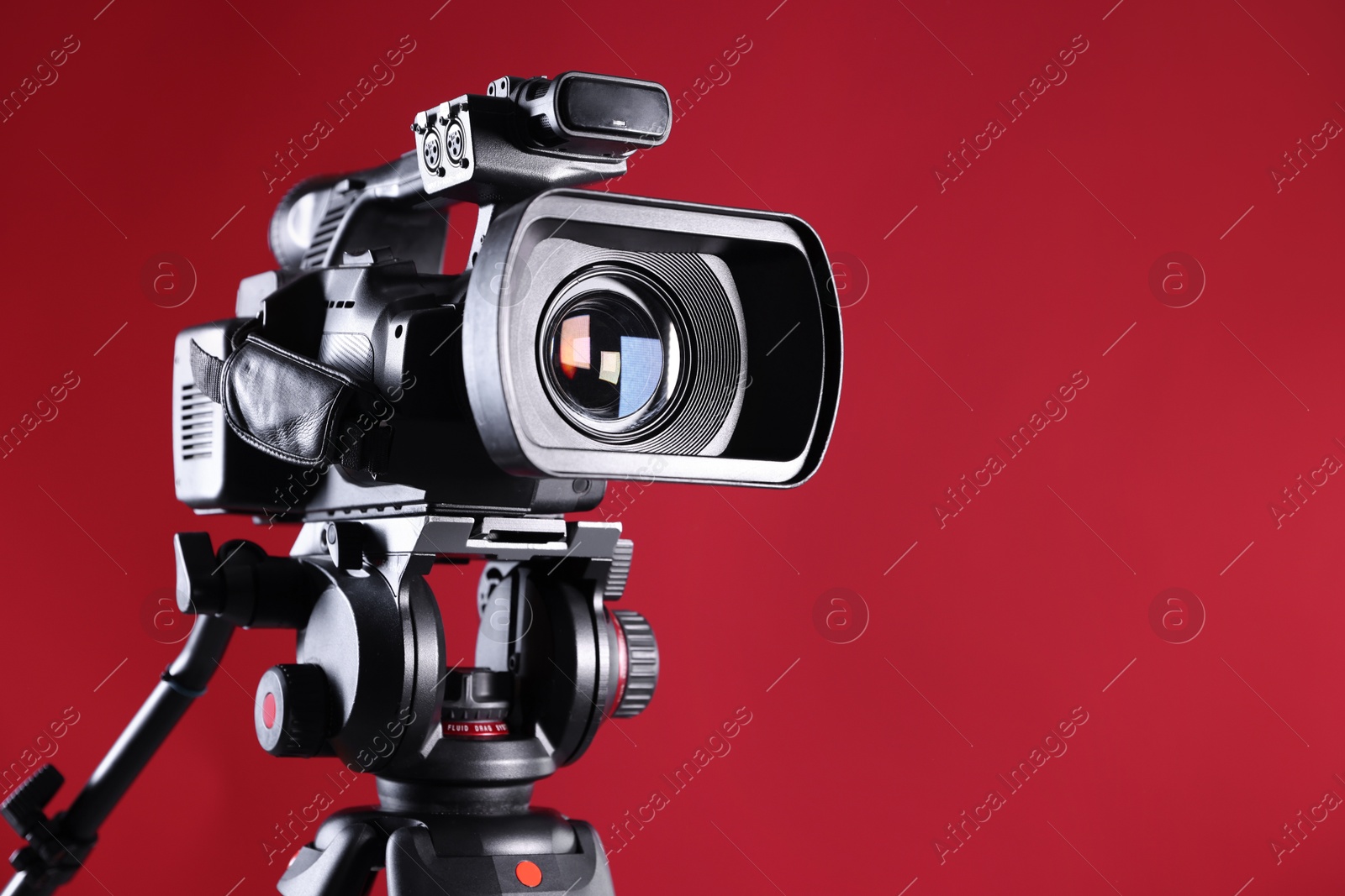 Photo of Modern video camera with tripod on red background, closeup. Space for text