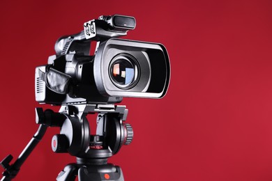 Modern video camera with tripod on red background, closeup. Space for text