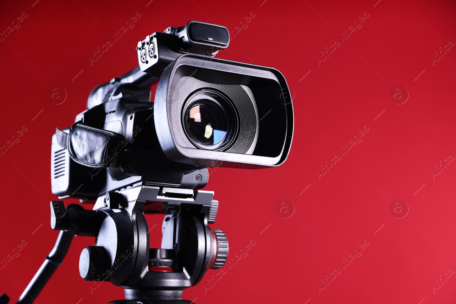 Photo of Modern video camera on red background, closeup. Space for text