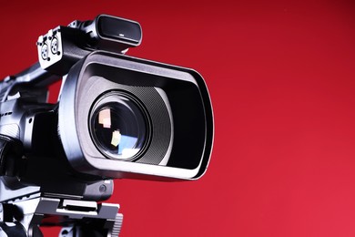 Modern video camera on red background, closeup. Space for text