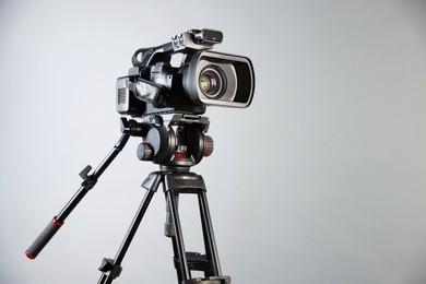 Modern video camera with tripod on light grey background, space for text