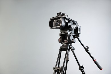 Photo of Modern video camera with tripod on light grey background, space for text