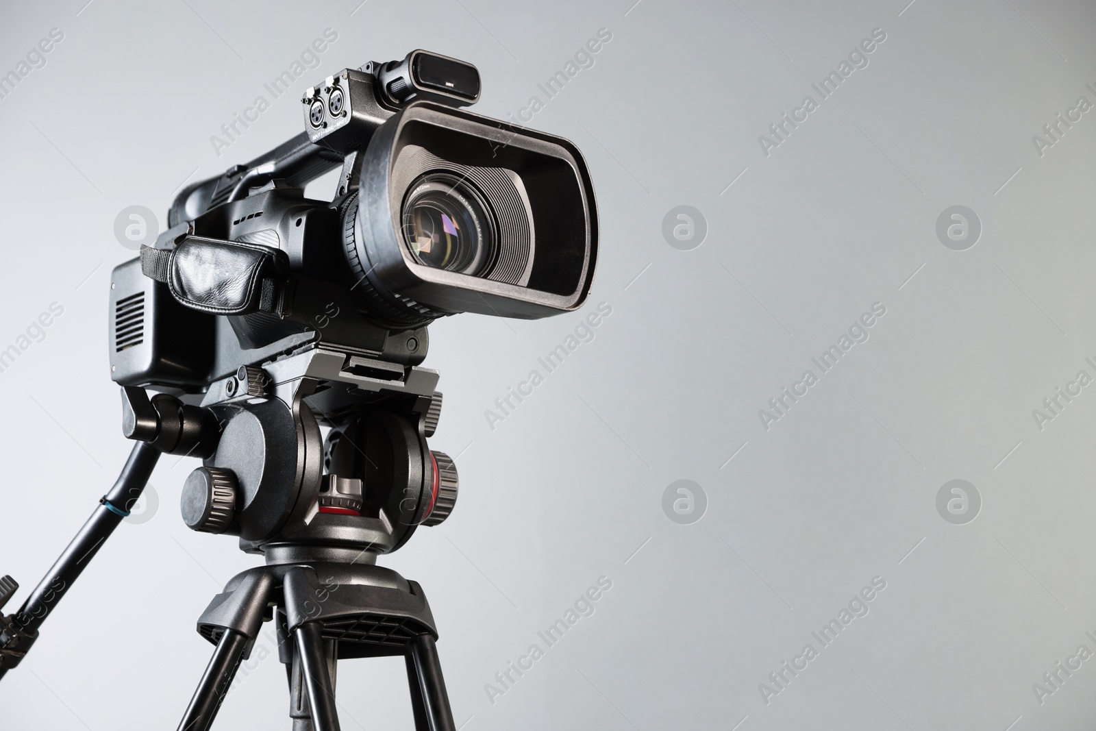 Photo of Modern video camera with tripod on light grey background, space for text