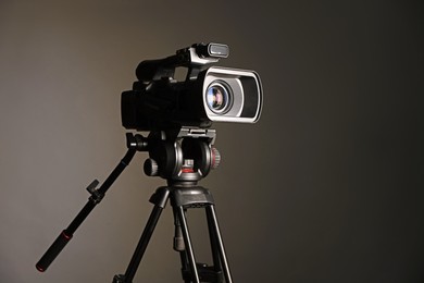 Modern video camera with tripod on grey background