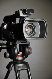 Modern video camera with tripod on grey background, closeup