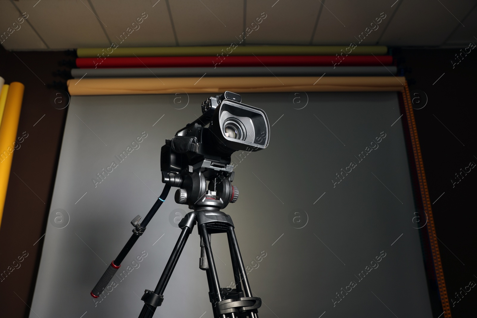 Photo of Modern video camera with tripod in studio, space for text