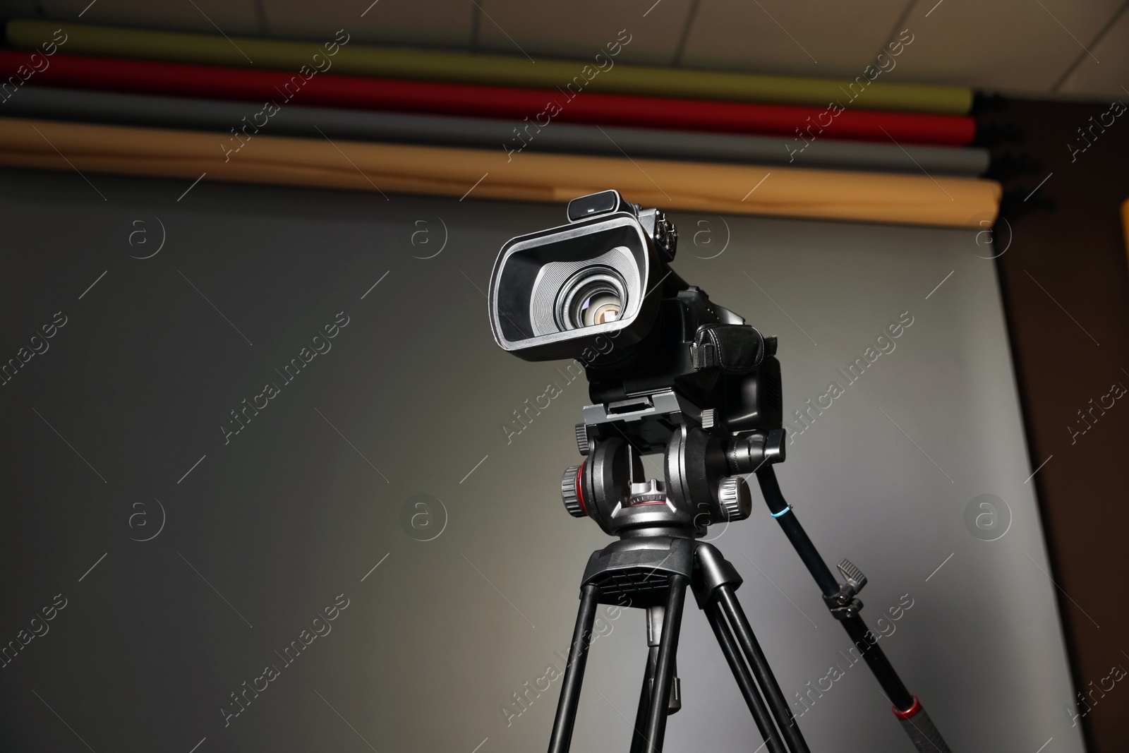 Photo of Modern video camera with tripod in studio, space for text