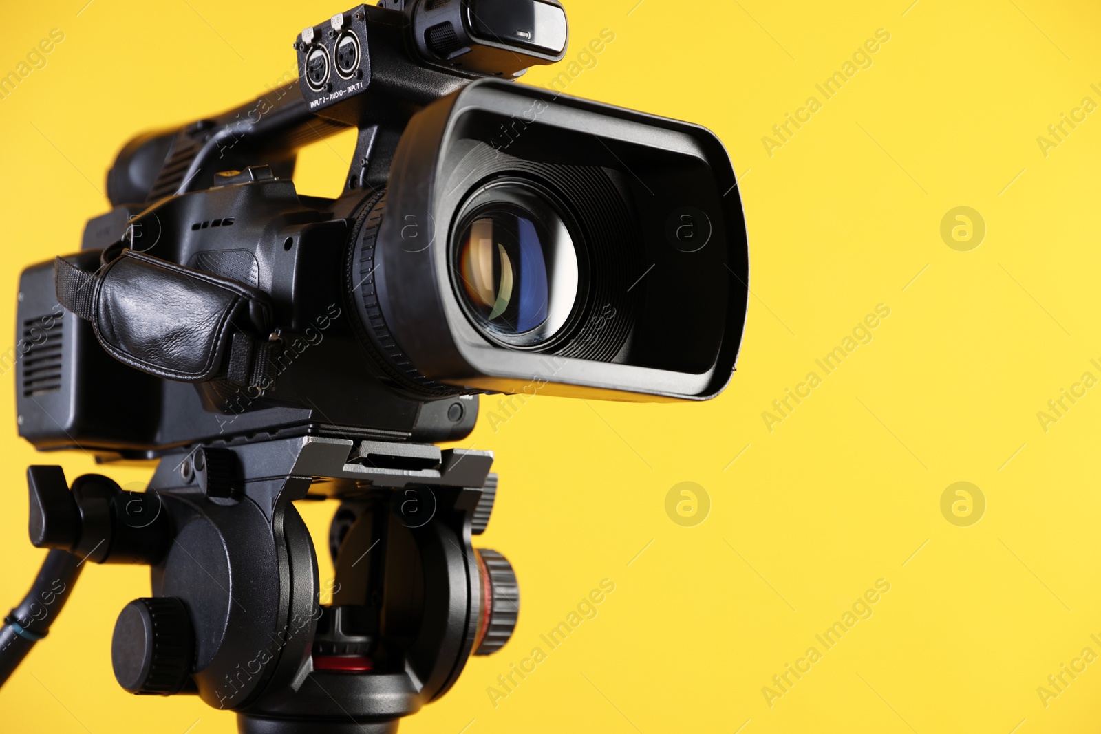 Photo of Modern video camera on yellow background, closeup. Space for text