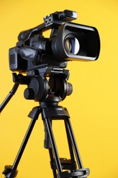 Photo of Modern video camera with tripod on yellow background