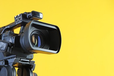 Photo of Modern video camera on yellow background, closeup. Space for text