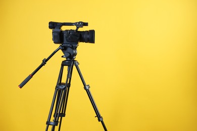 Modern video camera with tripod on yellow background, space for text