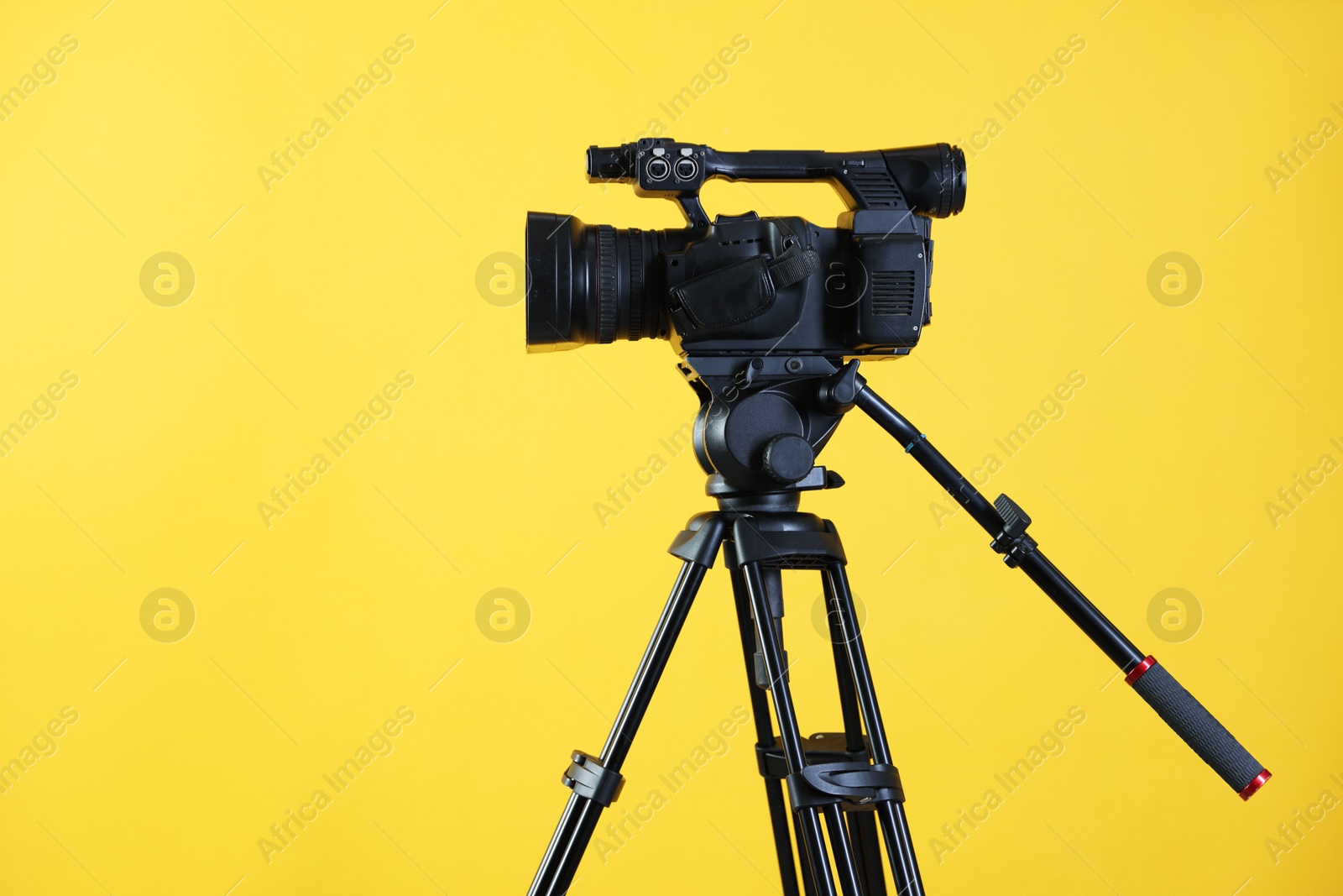 Photo of Modern video camera with tripod on yellow background, space for text