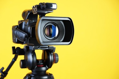 Photo of Modern video camera on yellow background, closeup. Space for text