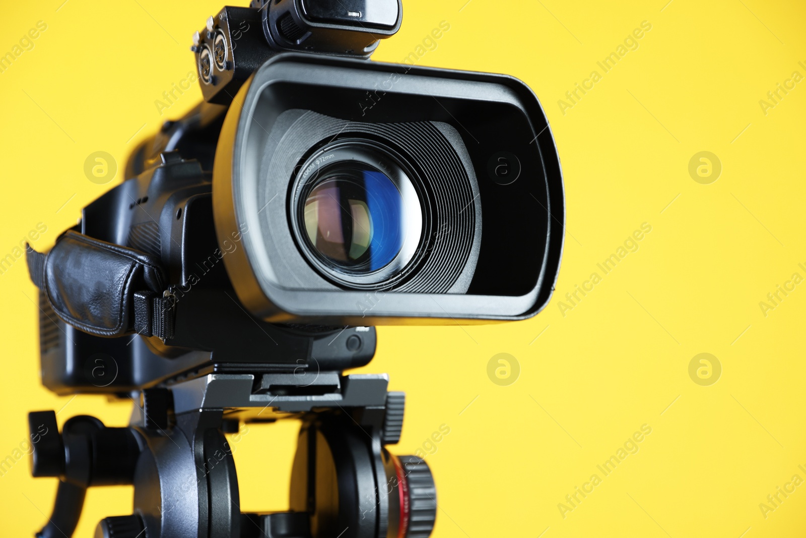 Photo of Modern video camera on yellow background, closeup. Space for text