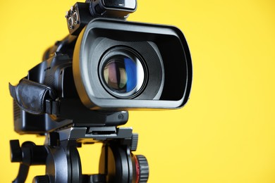 Photo of Modern video camera on yellow background, closeup. Space for text