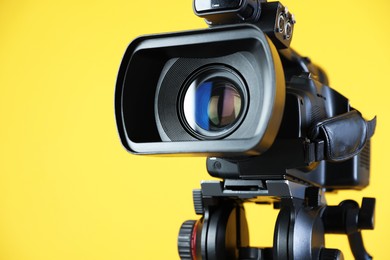 Photo of Modern video camera on yellow background, closeup. Space for text