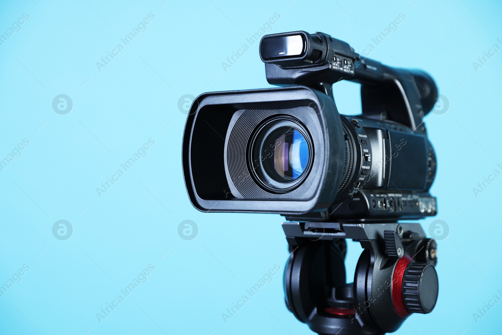 Photo of Modern video camera on light blue background, closeup. Space for text