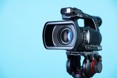 Modern video camera on light blue background, closeup. Space for text