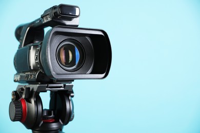 Photo of Modern video camera on light blue background, closeup. Space for text