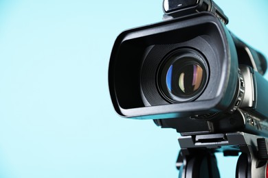 Modern video camera on light blue background, closeup. Space for text