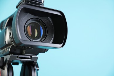 Modern video camera on light blue background, closeup. Space for text