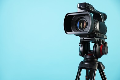 Modern video camera with tripod on light blue background, space for text