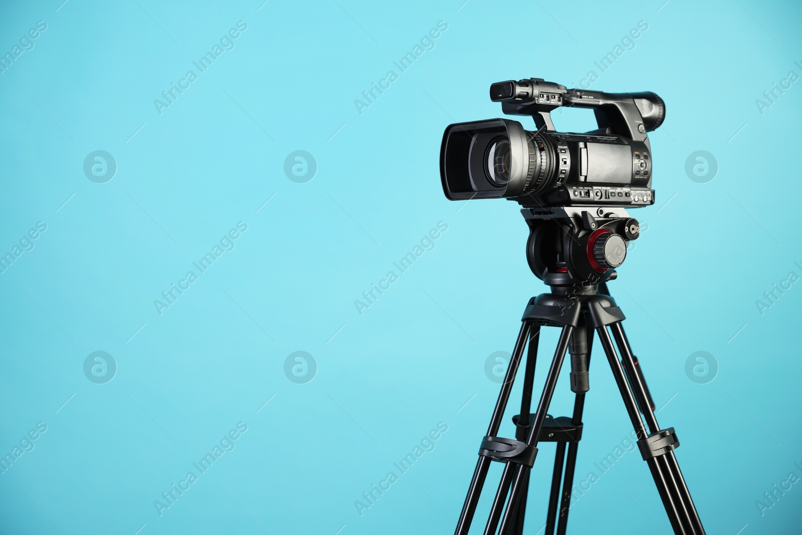 Photo of Modern video camera with tripod on light blue background, space for text