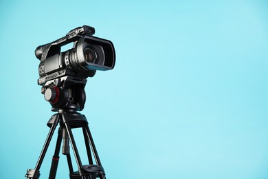 Photo of Modern video camera with tripod on light blue background, space for text