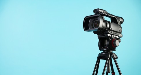 Modern video camera with tripod on light blue background, space for text