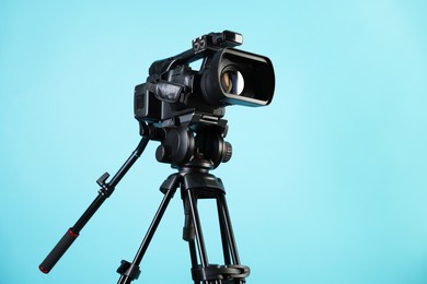 Modern video camera with tripod on light blue background, space for text