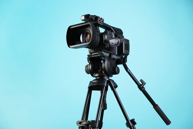 Modern video camera with tripod on light blue background, space for text