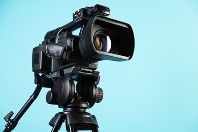 Photo of Modern video camera on light blue background, closeup. Space for text