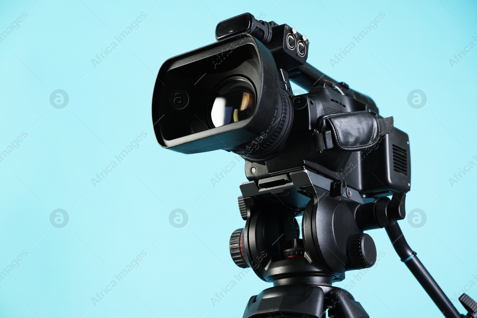 Photo of Modern video camera on light blue background, closeup. Space for text