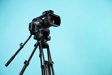 Photo of Modern video camera with tripod on light blue background, space for text