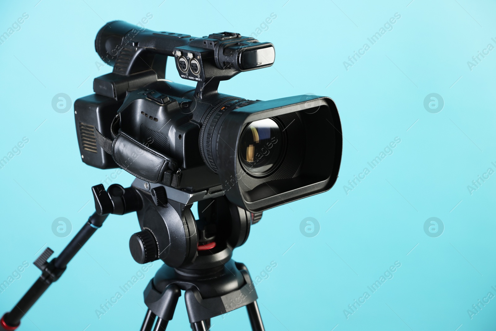 Photo of Modern video camera with tripod on light blue background, closeup. Space for text