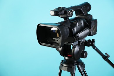 Photo of Modern video camera with tripod on light blue background, closeup. Space for text