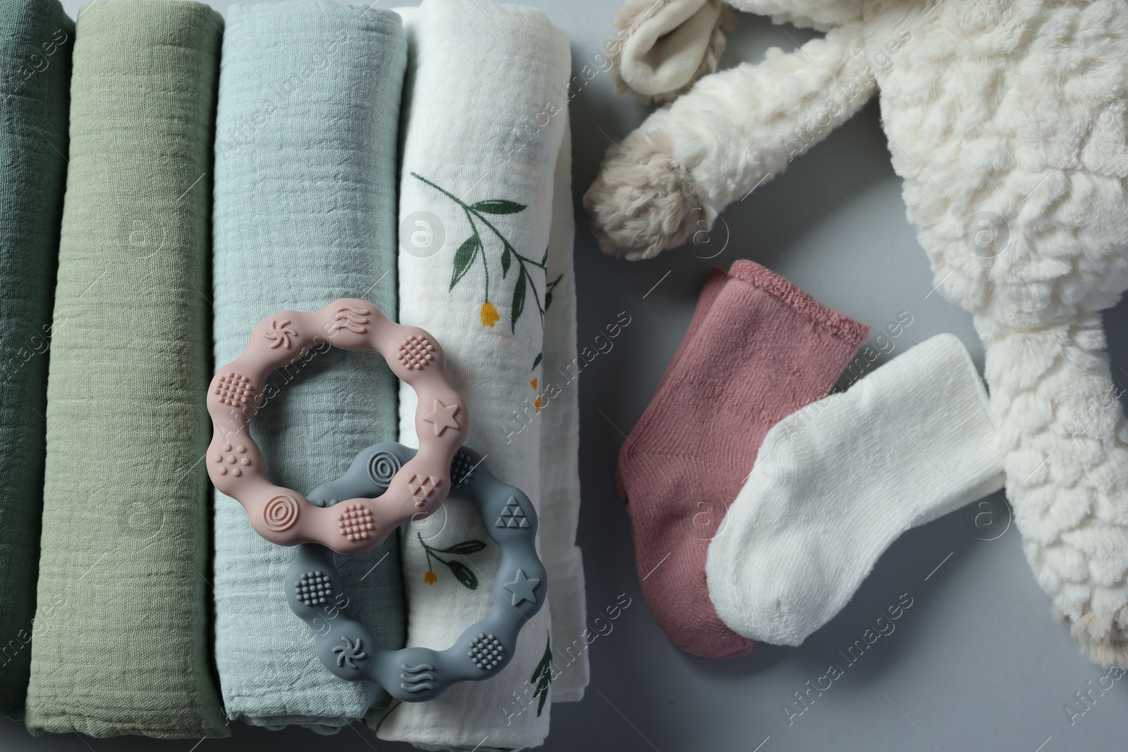 Photo of Rolled baby blankets, toy and teethers on light grey background, flat lay