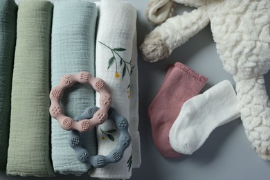 Rolled baby blankets, toy and teethers on light grey background, flat lay