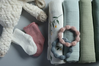 Photo of Rolled baby blankets, toy and teethers on light grey background, flat lay