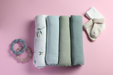 Photo of Rolled baby blankets, teethers and socks on pink background, flat lay