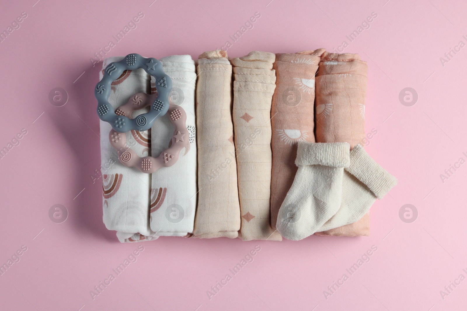 Photo of Rolled baby blankets, teethers and socks on pink background, flat lay