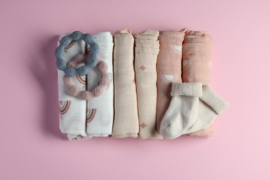 Rolled baby blankets, teethers and socks on pink background, flat lay