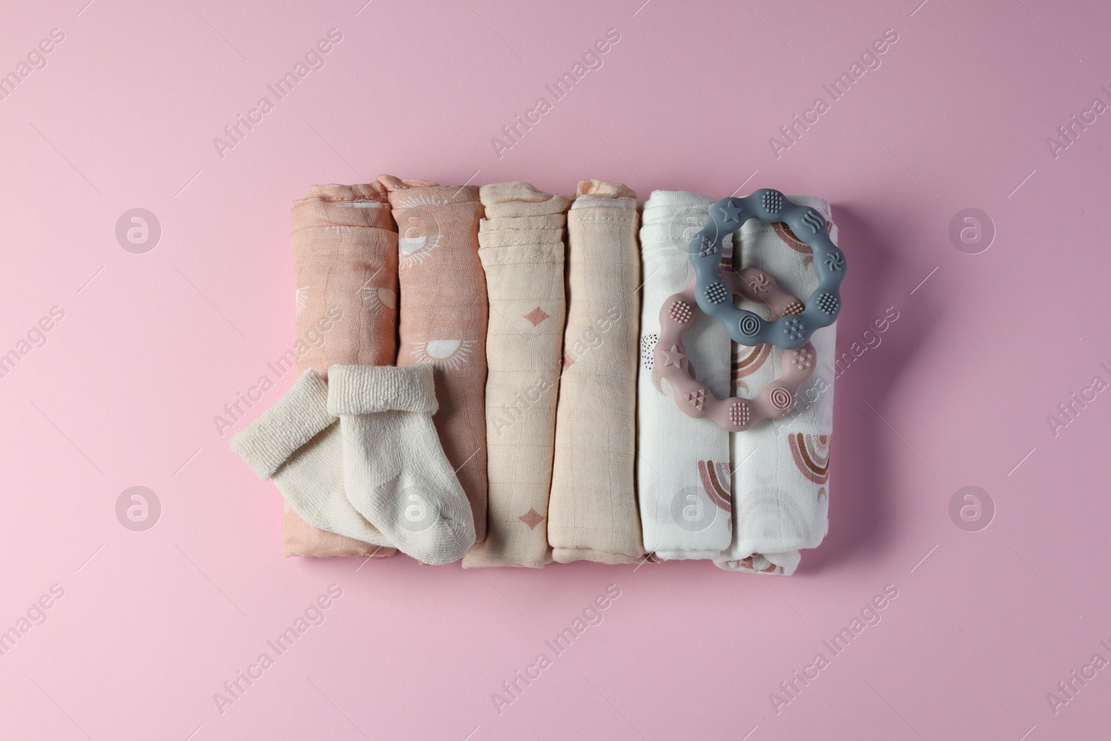 Photo of Rolled baby blankets, teethers and socks on pink background, flat lay