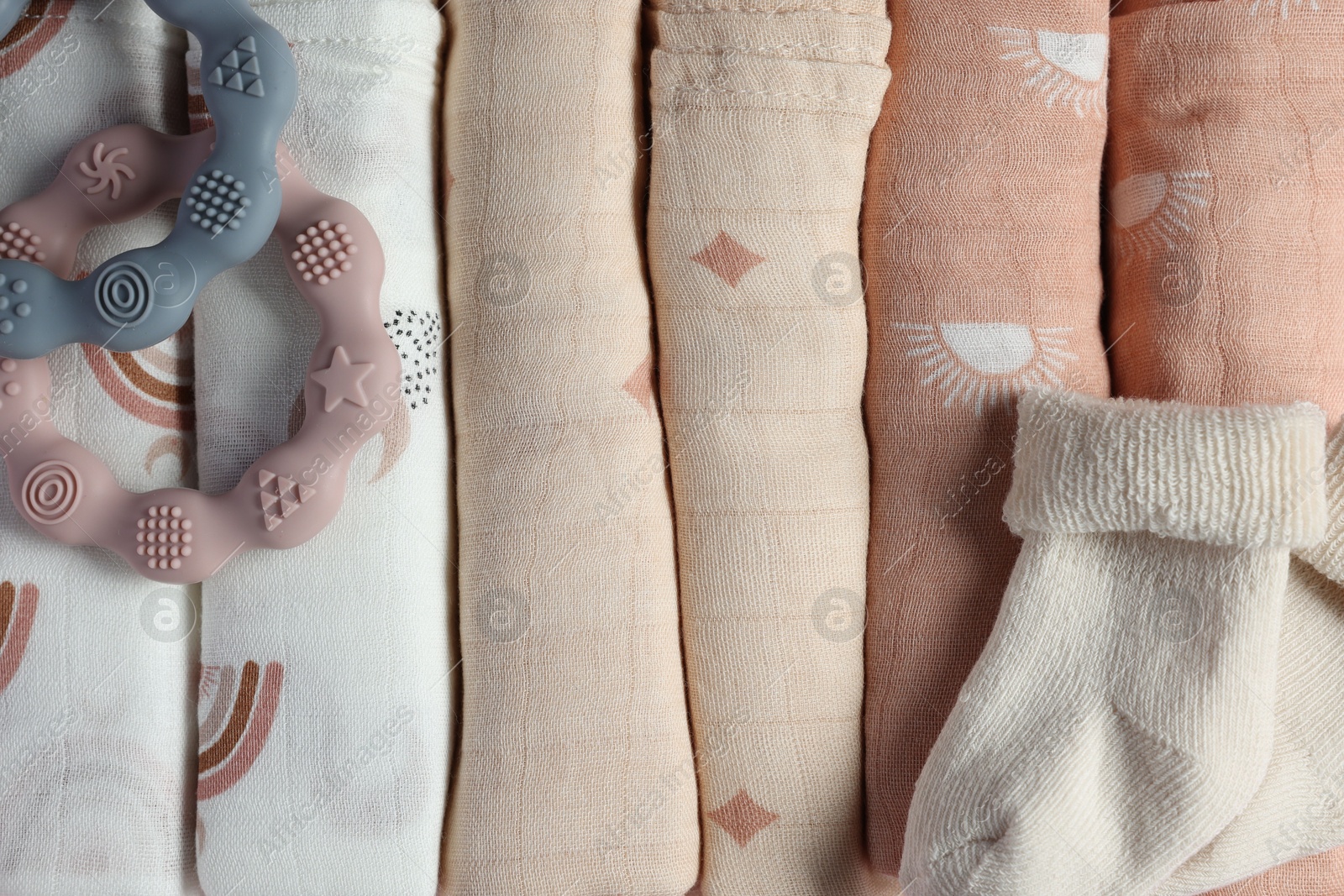 Photo of Rolled baby blankets, teethers and socks as background, top view