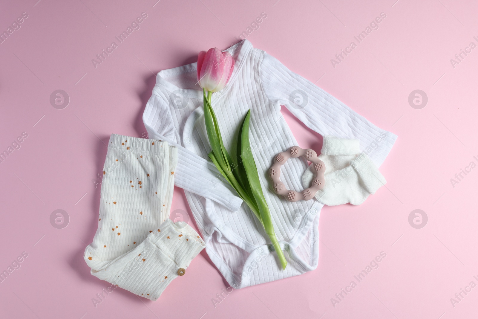 Photo of Baby clothes, socks, teether and tulip flower on pink background, flat lay