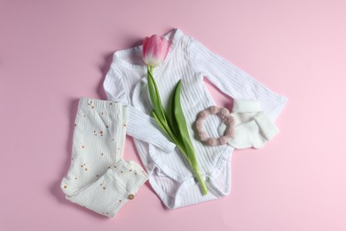 Baby clothes, socks, teether and tulip flower on pink background, flat lay