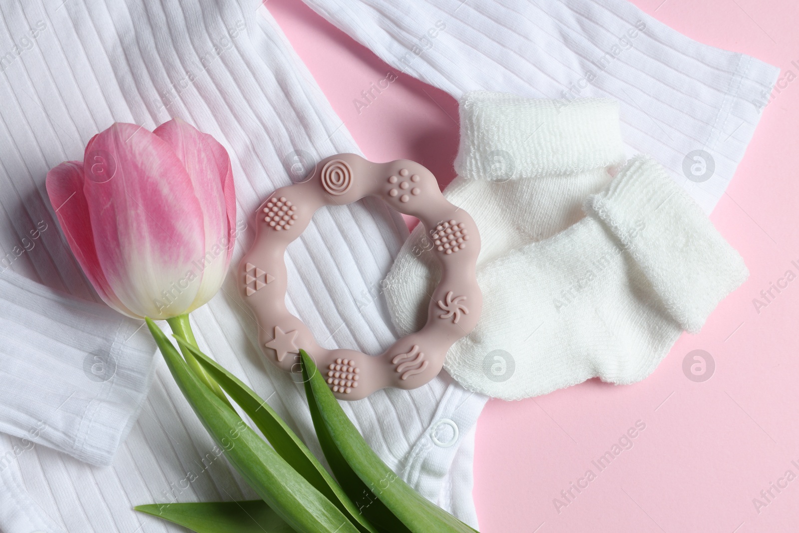 Photo of Baby onesie, socks, teether and tulip flower on pink background, flat lay